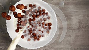 Preparing tasty breakfast of chocolate cornflakes in form of balls and milk in slowmo