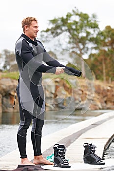 Preparing to get wakeboarding. Young man putting on his wetsuit before engaging in some watersports.