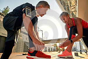 Preparing to run. Active and healthy middle-aged couple in sports clothing tying shoelaces before jogging outdoors