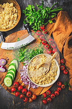 Preparing traditional oriental salad Tabouleh with couscous or bulgur, ingredients on cutting board