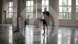 Preparing for training in empty studio with panoramic windows. Young woman with dreadlocks and man rolls apart yoga mat