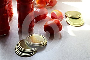 Preparing vegetables for the winter: ripe tomatoes, seaming lids, glass jars with tomatoes on the kitchen table