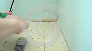 Preparing the wall for fixing baseboard. Close-up of the hand of a female worker with assembly glue gun and putty knife