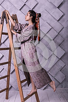 Prepossessing poser wearing dress standing on ladder during studio shooting