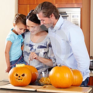 Prepping the pumpkin for Halloween. A young mother and father standing with their young daughter in a kitchen preparing