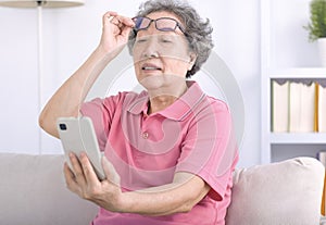 Presbyopia, senior asian woman holding eyeglasses having problem with vision problem trying to read text on mobile phone photo