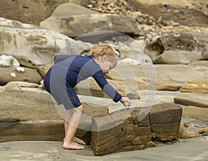 Preschool aged boy in a blue swimming suit picking up a shell at some tide pools