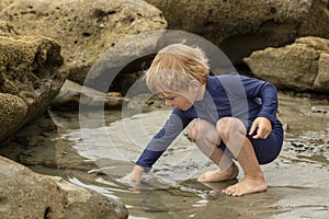 Preschool aged boy in a blue swimming suit playing in tidepools at the beach