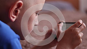 Preschool boy at Home is Lying on the bed, using a Smartphone. Child playing video games on a cellphone, Browses