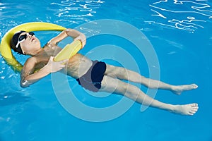 Preschool boy learning to swim in pool with foam noodle