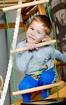 Preschool boy makes exercises on a gym wall bars