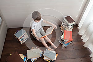 A preschool boy is sitting on books.