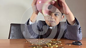 Preschool boy in a suit trying to get more money from an empty piggy bank. Recession and negative returns on investment