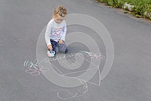 Preschool caucasian girl drawing a house with chalks