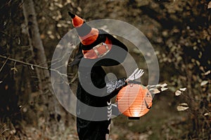 Preschool child with halloween costume and jack` o` lantern in a forest, scary skelleton