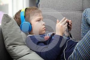 Preschool child listens to music on a smartphone while lying at home on the bed, boy plays on the phone