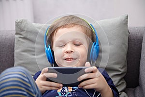 Preschool child listens to music on a smartphone while lying at home on the bed, boy plays on the phone