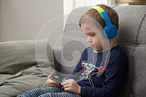 Preschool child listens to music on a smartphone while lying at home on the bed, boy plays on the phone