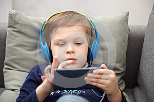 Preschool child listens to music on a smartphone while lying at home on the bed, boy plays on the phone