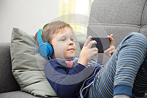 Preschool child listens to music on a smartphone while lying at home on the bed, boy plays on the phone