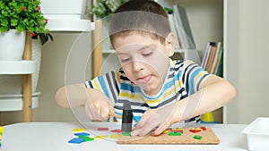 A preschool child plays with a mosaic, builds figures on a board, hammering nails with a hammer on multi-colored parts