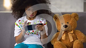 Preschool curly african girl studying letters on smartphone, educational apps