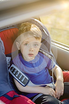 Preschool cute 3-4 years old boy sitting in safety car seat and crying during family travel by car, bad mood, negative emotion,