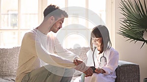 Preschool daughter wearing white coat uniform playing doctor with father