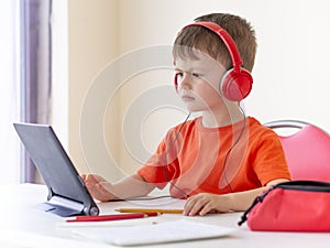 Preschool e-learning concept. Boy wears headphones and Looking lecture at the tablet