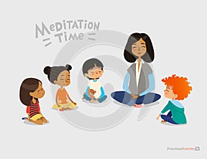 Preschool female teacher and smiling kids sitting in circle on floor and doing yoga exercise. Meditation lesson in kindergarten co