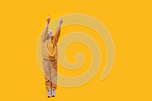 Preschool girl raised hands up and points index fingers up. Copy space, mock up. Vertical frame, child in yellow clothes