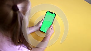 Preschool Girl Use Smartphone With a Green Screen Layout. Chroma key mock-up on smartphone in hand. Color Key. Watching