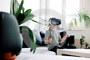 Preschool girl with virtual reality headset sitting on sofa