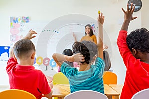 Preschool kid raise arm up to answer teacher question on whiteboard in classroom,Kindergarten education concept