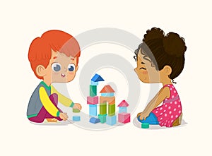 Preschool Red Hair Boy and African American Girl Kids playing with wooden bricks and blocks together in kindergarten