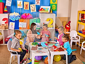 Preschool scissors in kids hands cutting paper with techer in class.