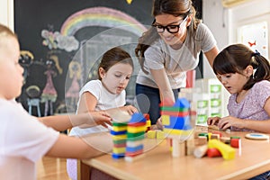 Preschool teacher with children playing with colorful wooden didactic toys at kindergarten