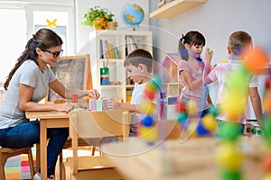 Preschool teacher with children playing with colorful wooden didactic toys at kindergarten