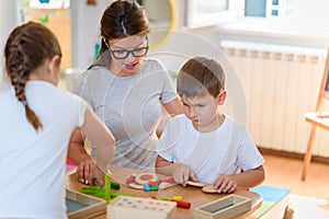 Preschool teacher with children playing with colorful wooden didactic toys at kindergarten