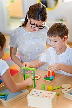 Preschool teacher with children playing with colorful wooden didactic toys at kindergarten