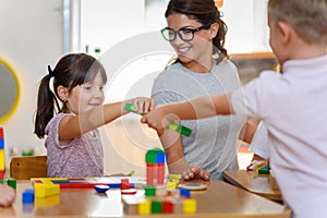 Preschool teacher with children playing with colorful wooden didactic toys at kindergarten