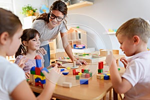 Preschool teacher with children playing with colorful wooden didactic toys at kindergarten