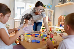 Preschool teacher with children playing with colorful wooden didactic toys at kindergarten