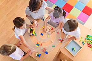 Preschool teacher with children playing with colorful wooden didactic toys at kindergarten