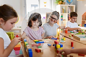 Preschool teacher with children playing with colorful wooden didactic toys at kindergarten photo