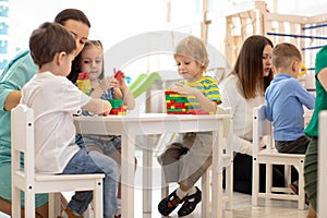 Preschool teacher with children playing with colorful wooden educational toys at kindergarten