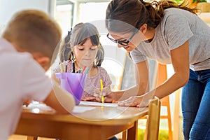 Preschool teacher looking at smart child learning to write and draw photo