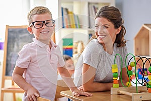 Preschool teacher with smart boy playing with colorful didactic toys at kindergarten