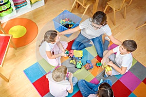 Preschool teacher talking to group of children sitting on a floor at kindergarten