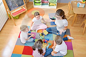 Preschool teacher talking to group of children sitting on a floor at kindergarten